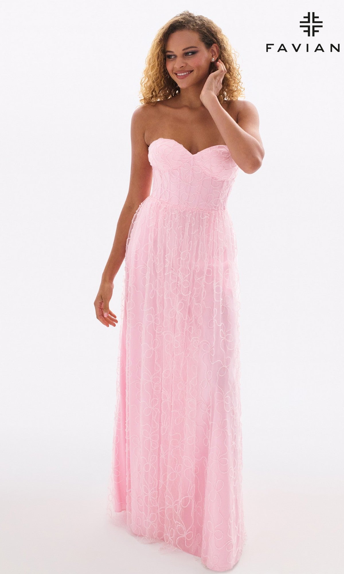 A woman models the Faviana 11418 long prom dress, featuring a strapless corset bodice and floor-length pink lace, standing against a white background with the Faviana logo in the top right corner.